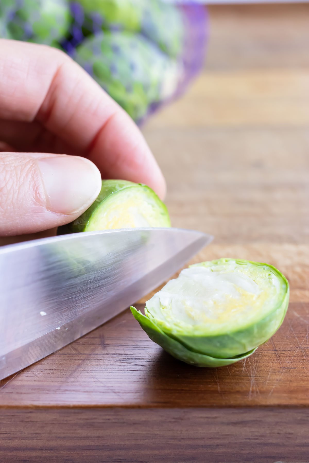 Brussels sprouts are chopped with a large knife on a cutting board.