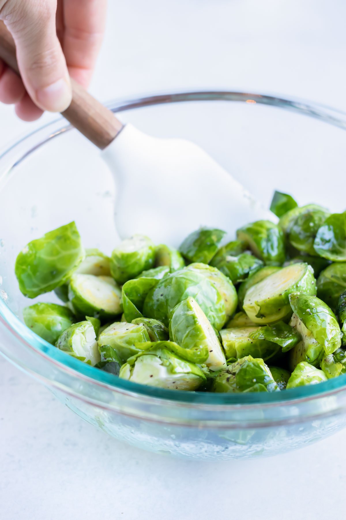 Chopped brussels sprouts are coated with oil mixture in a glass bowl.