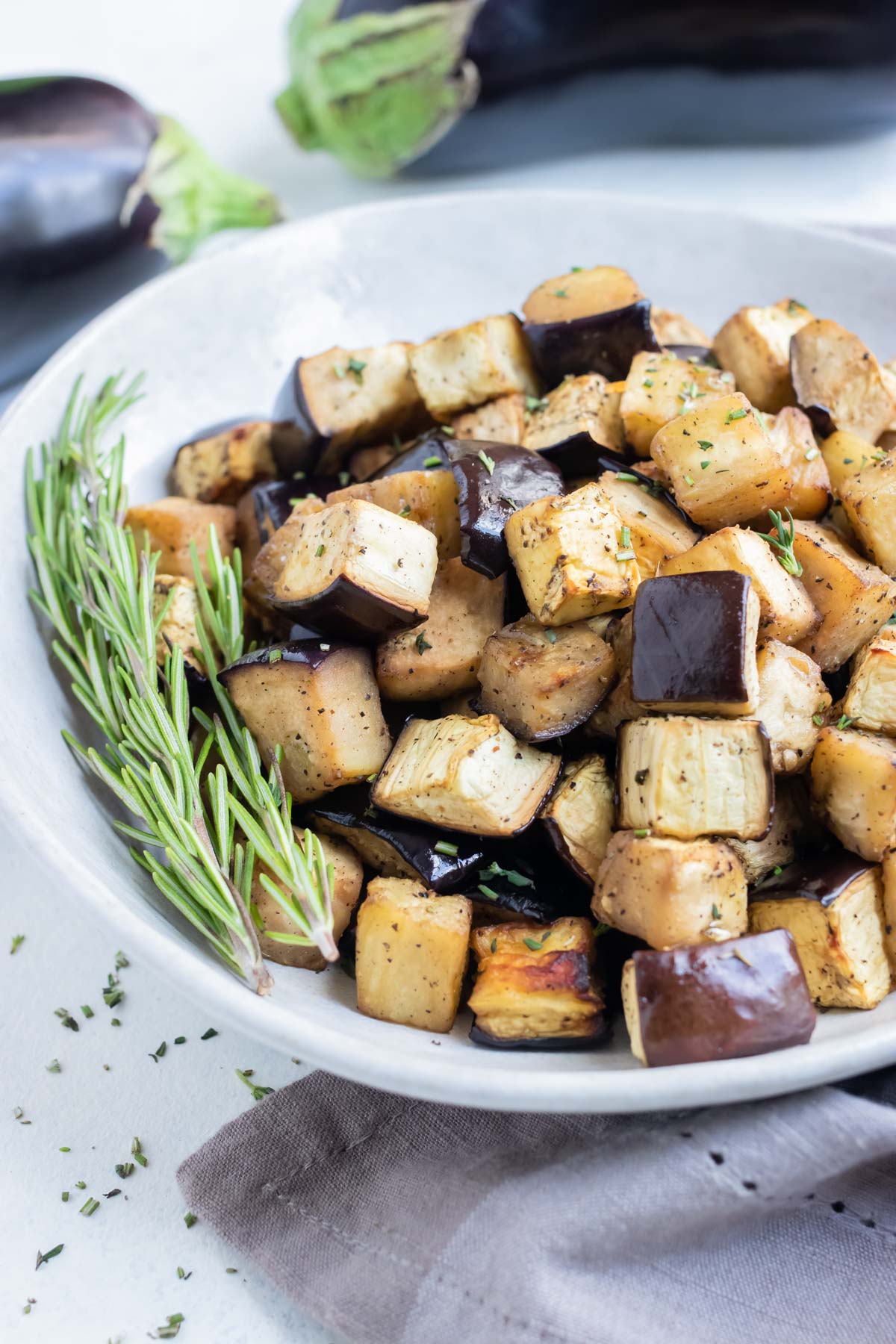 Eggplant is served with fresh herbs from a white bowl.