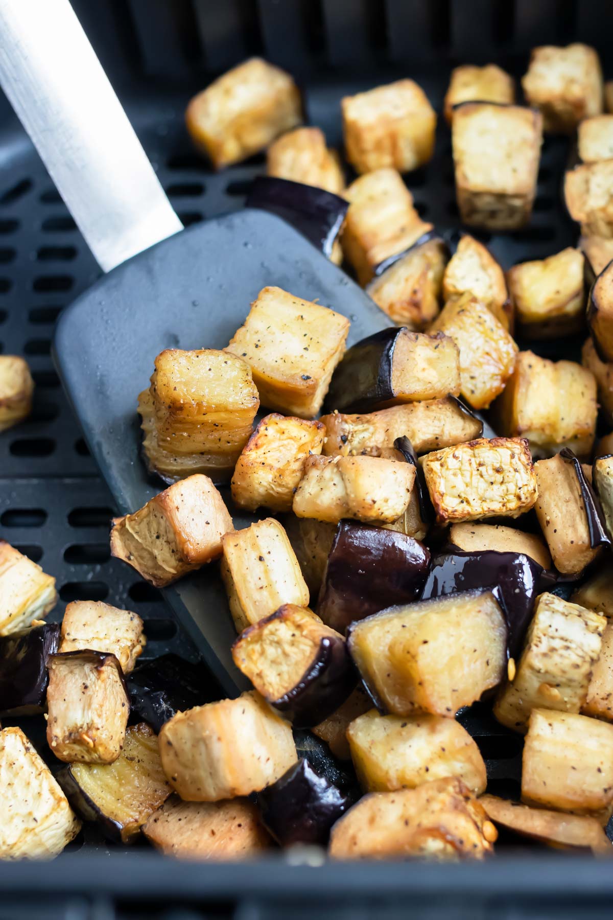 A spatula is used to remove the eggplant from the air fryer.