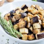 Crispy cubed eggplant is enjoyed from a white bowl with fresh herbs.