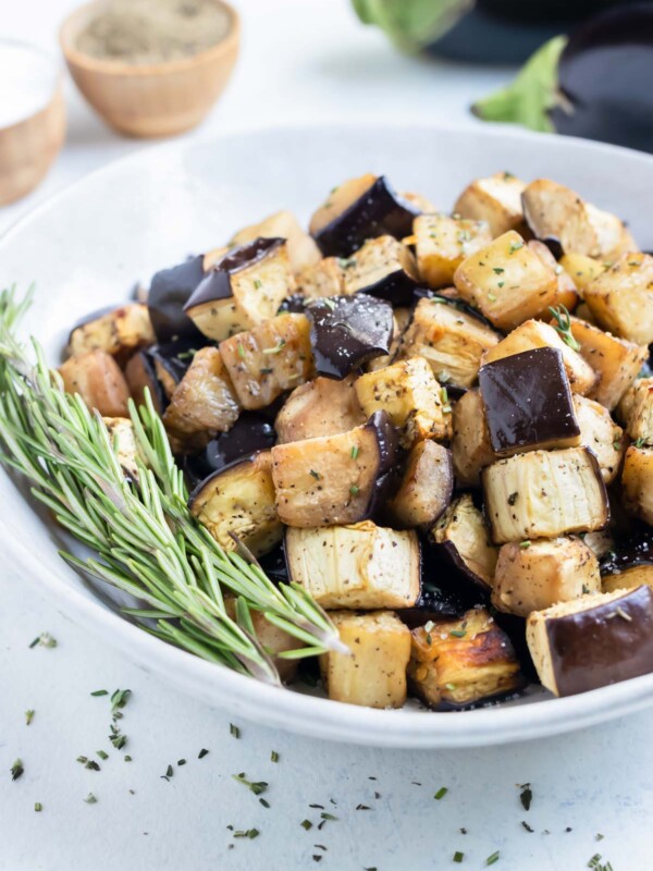 Crispy cubed eggplant is enjoyed from a white bowl with fresh herbs.