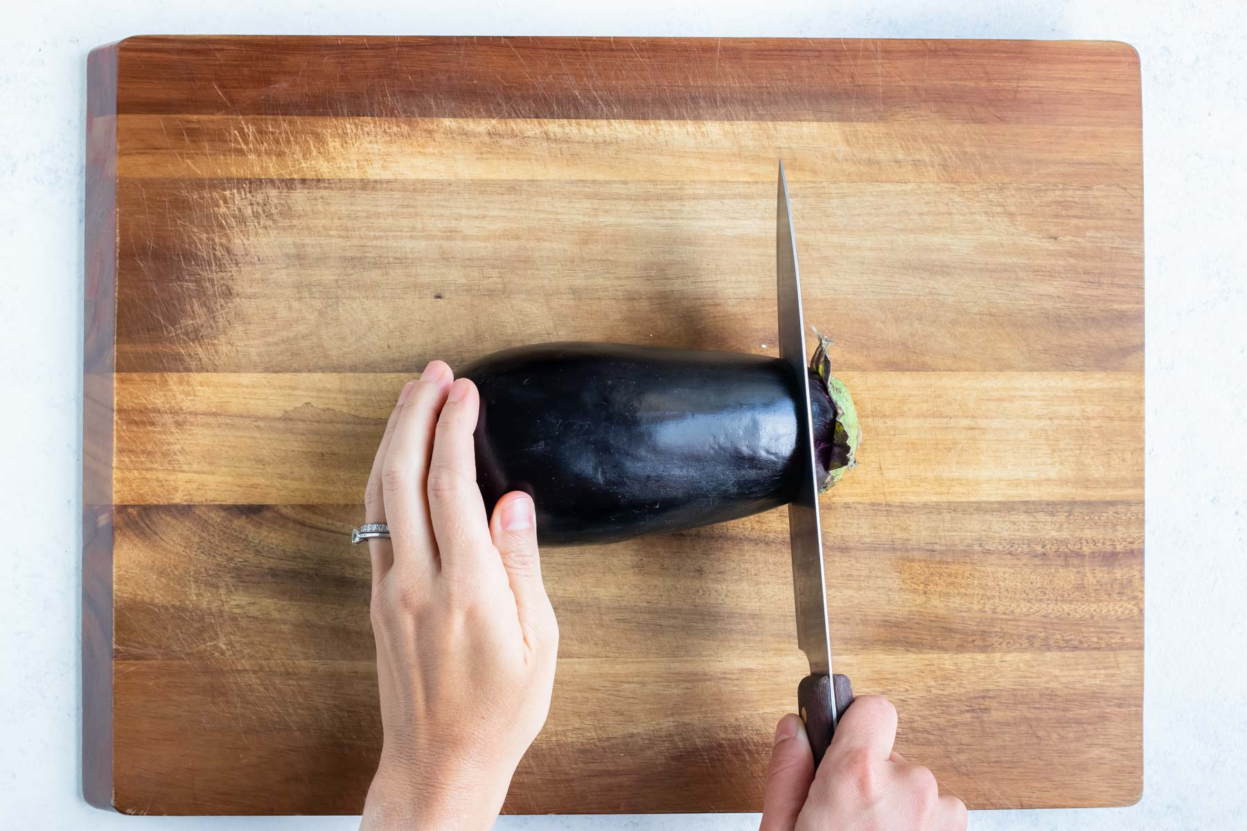 The top of the eggplant is removed with a knife.