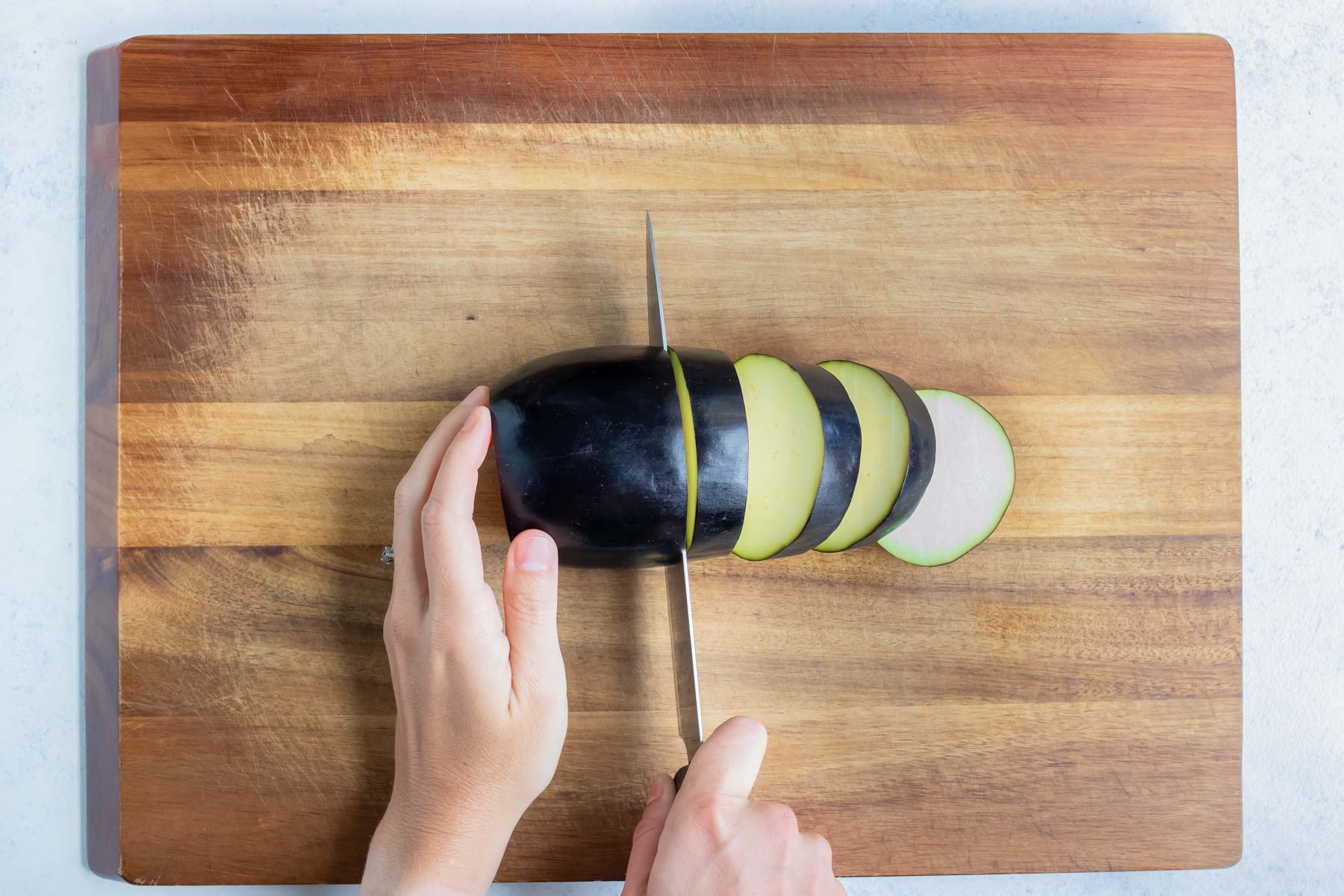 A large knife slices the eggplant.