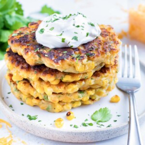 A white plate with sweet and savory corn fritters with a fork.