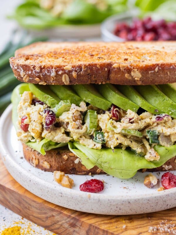 A curried chicken salad with cranberries and walnuts is served on bread with avocado for a sandwich.