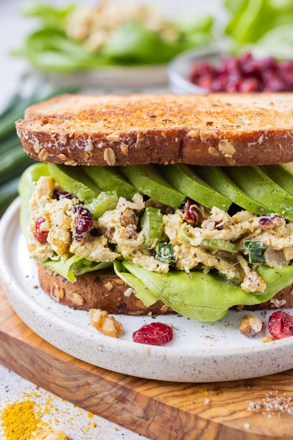 A curried chicken salad with cranberries and walnuts is served on bread with avocado for a sandwich.