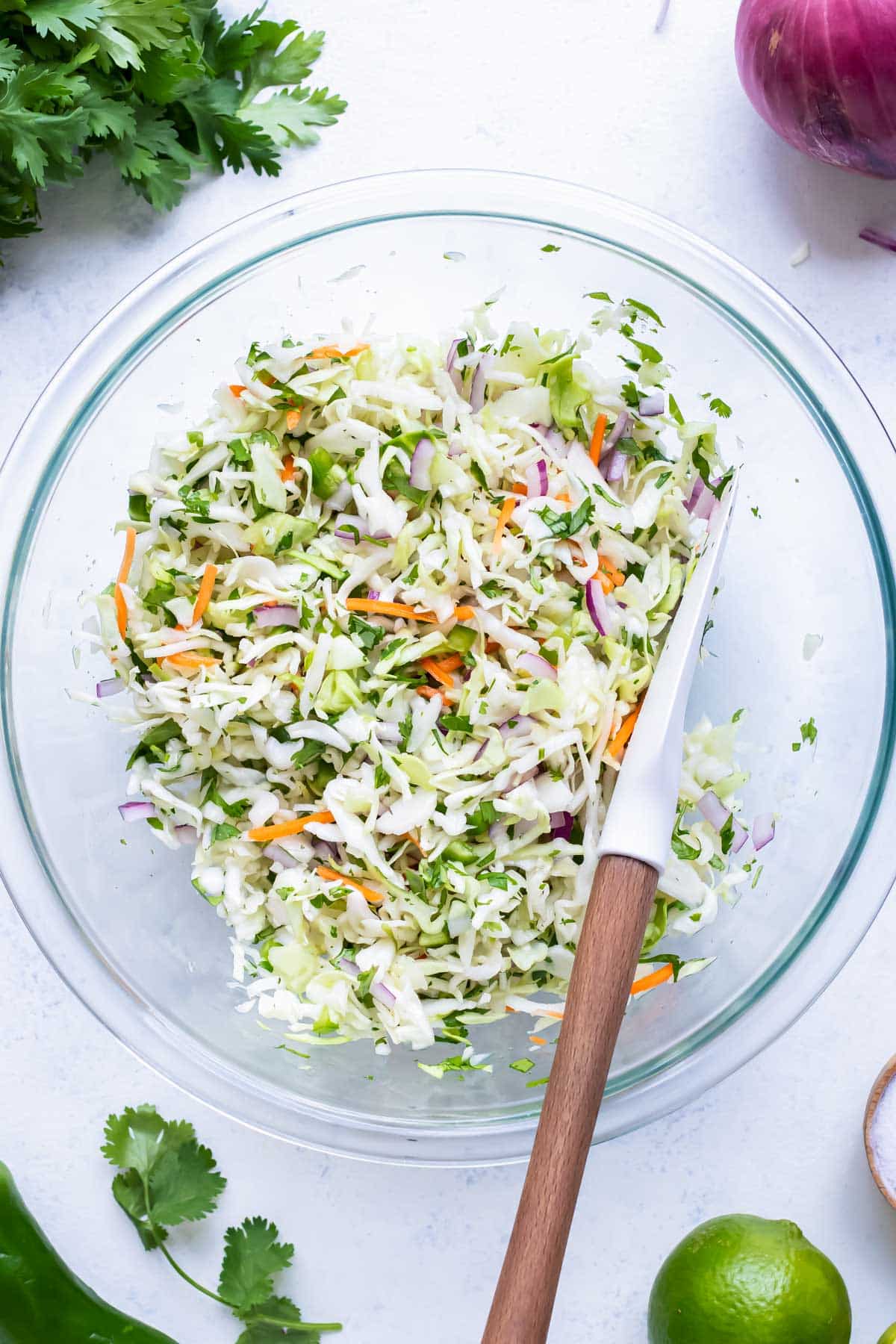 A glass bowl is filled with cabbage and other ingredients for this taco slaw.