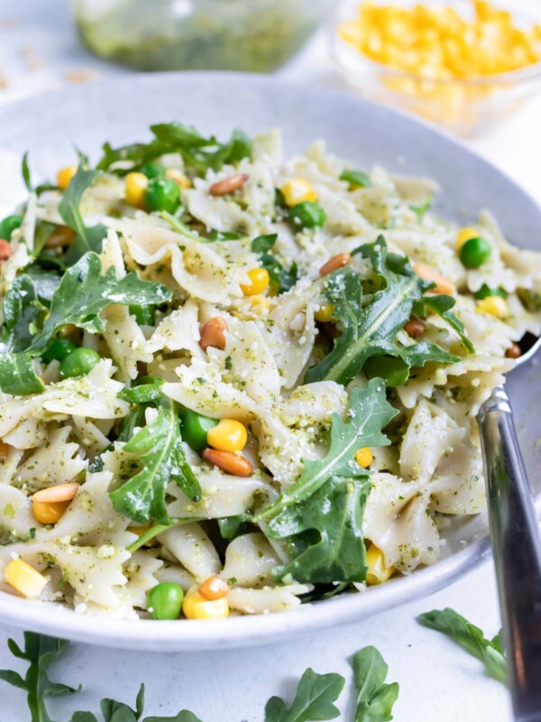 Cold pesto pasta salad is served from a white bowl with a metal spoon.