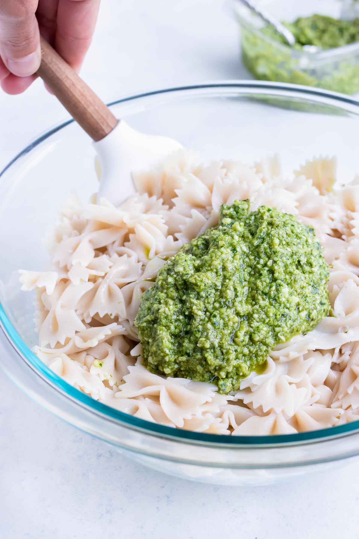 Basil pesto is added to a bowl of cooked pasta.