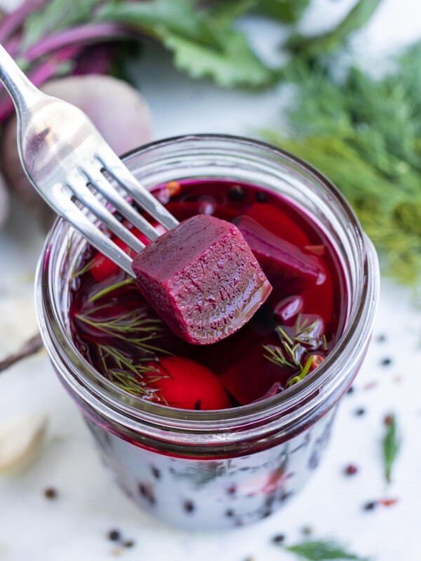 A fork scoops a pickled beet cube out of the jar.