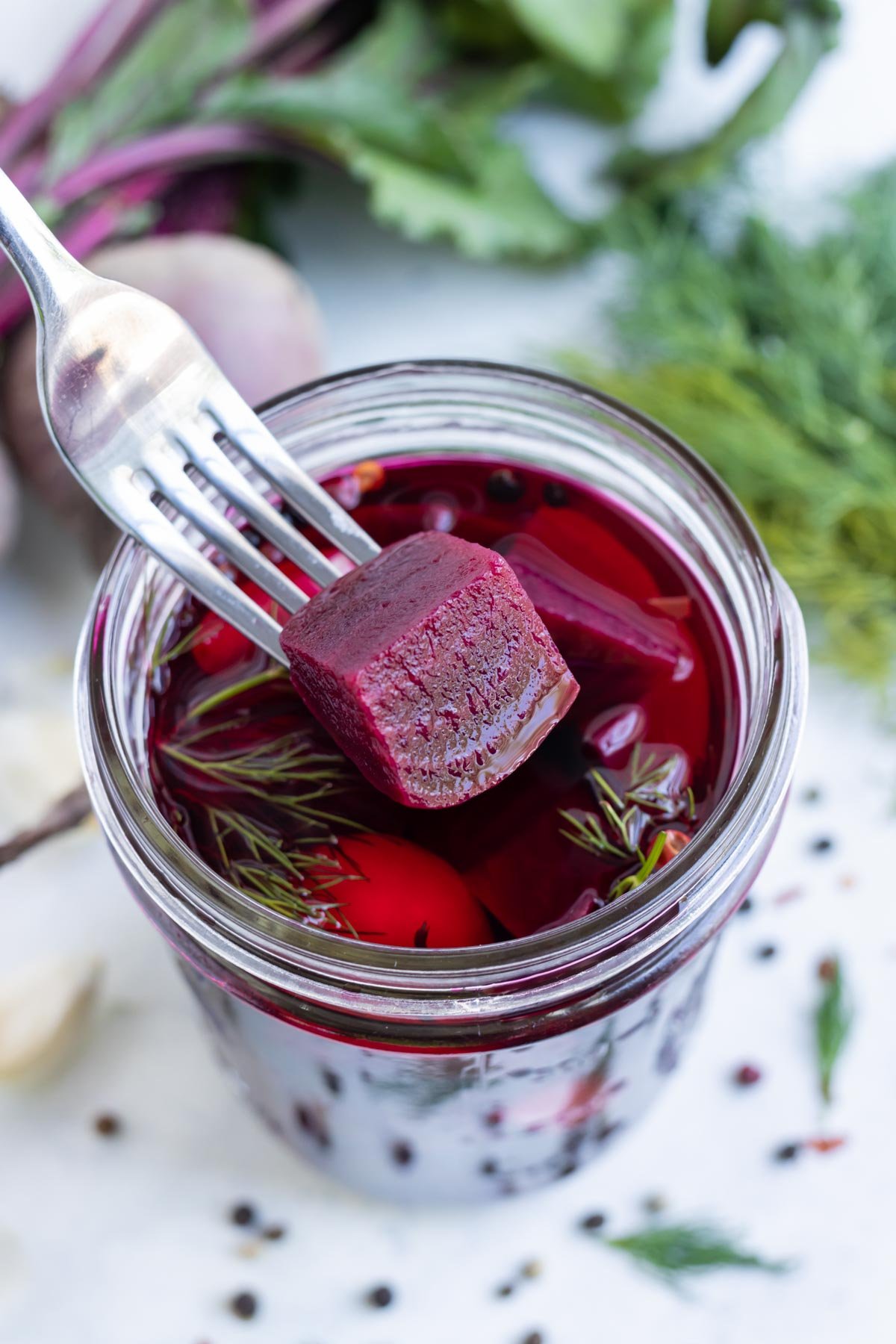 A fork scoops a pickled beet cube out of the jar.