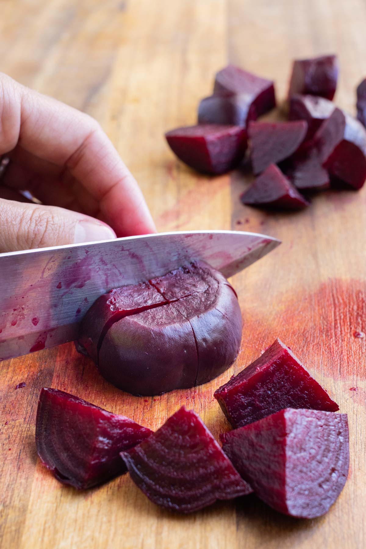 Roasted beets are sliced with a knife on a cutting board.