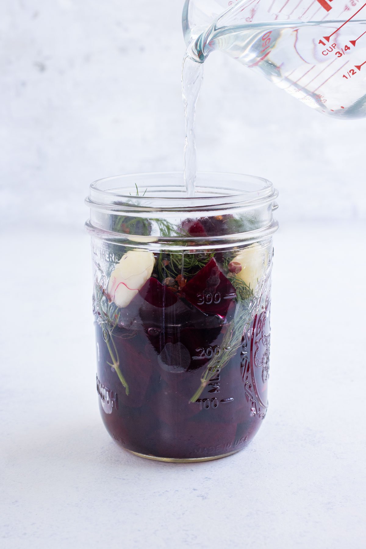 Brining solution is poured into a jar with roasted beets.