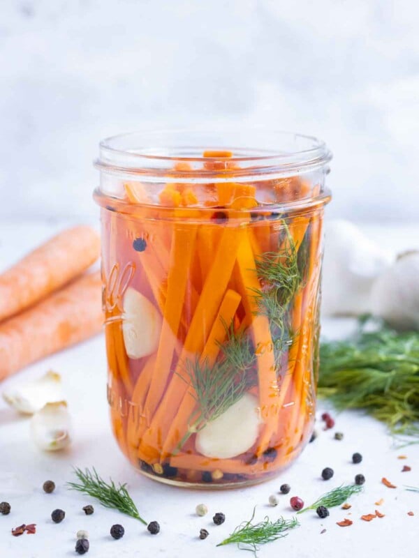 A jar with carrots, garlic, dill, and peppercorns with brining solution.