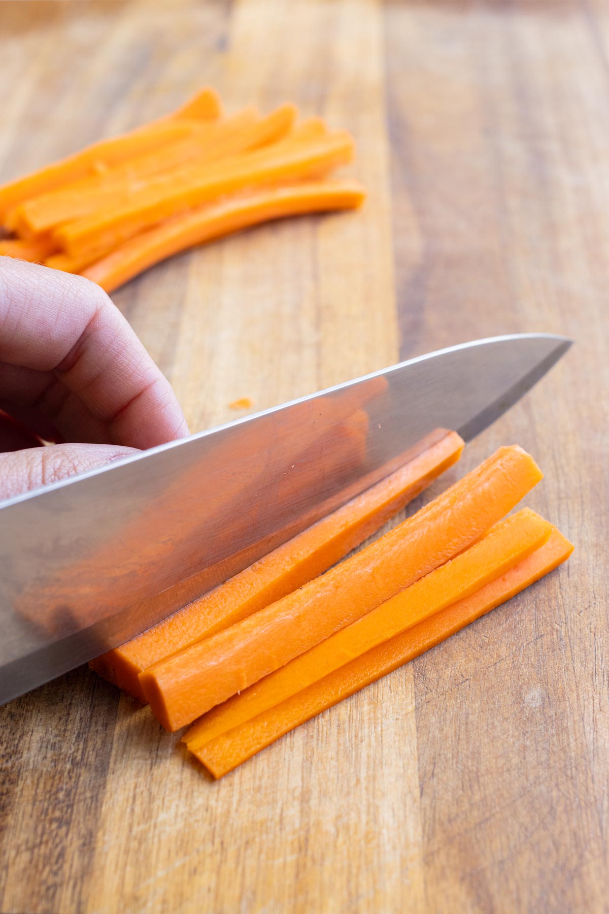 A sharp knife slices a carrot into sticks.