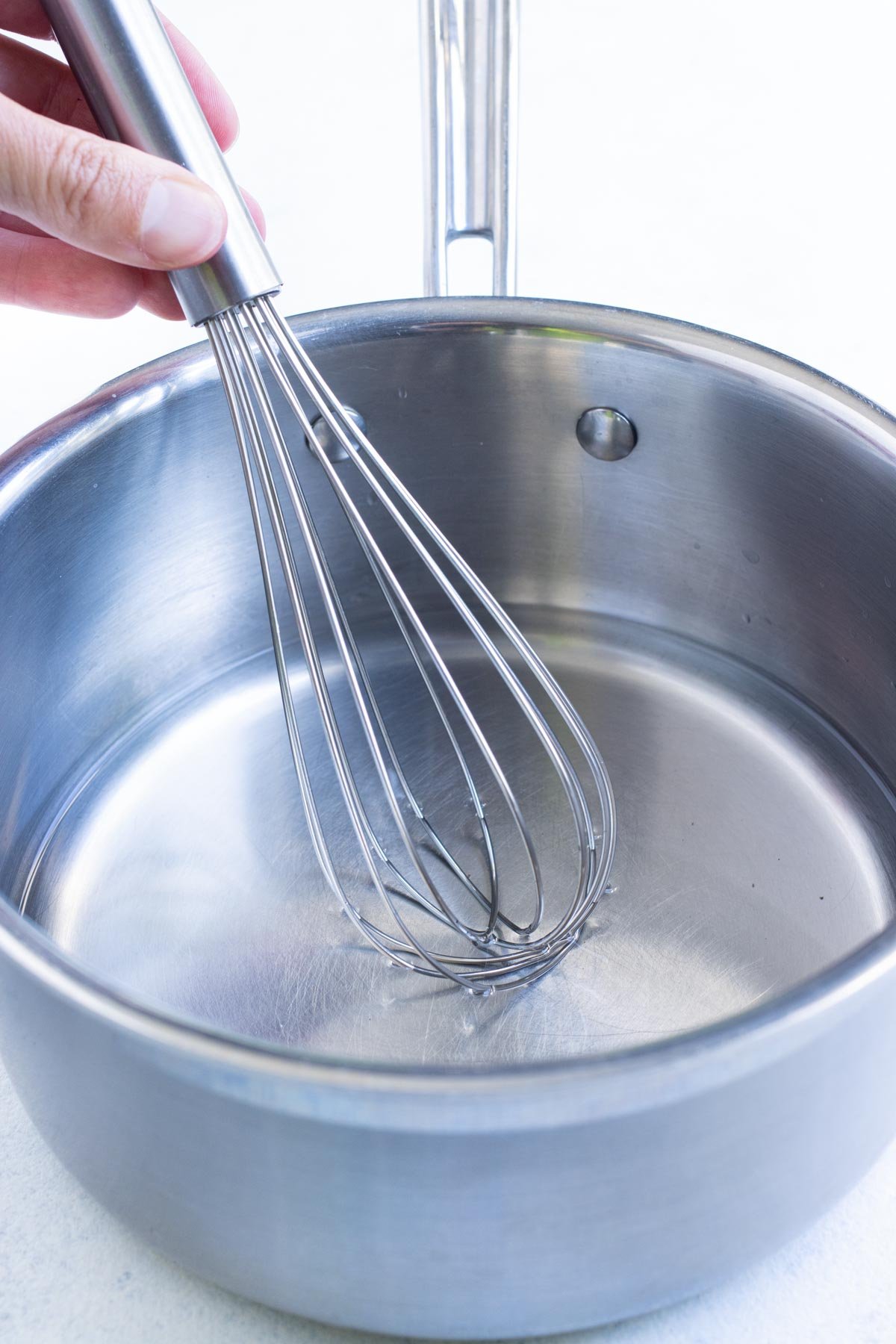 A whisk stirs brining solution in a saucepan.