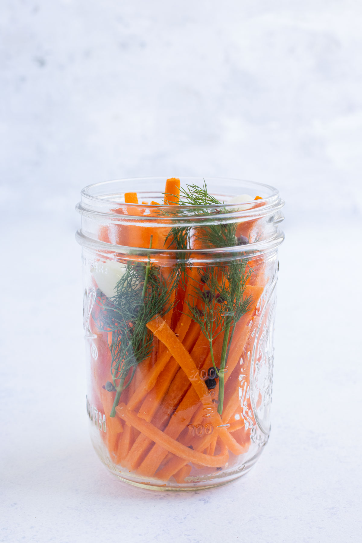 Carrots, dill, garlic, and peppercorns are in a glass jar.