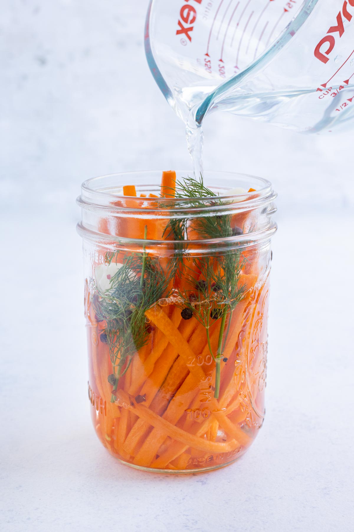 Brining solution is poured over carrots in a jar.