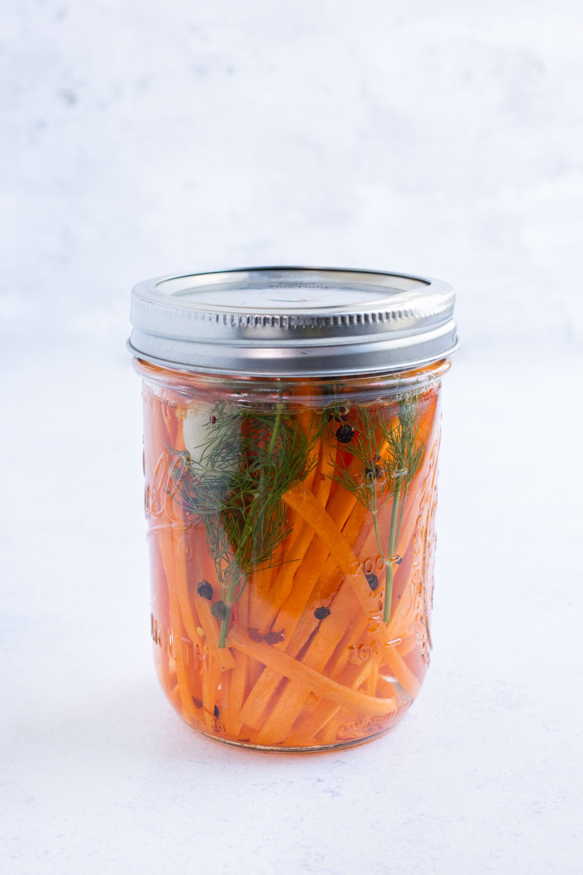 A lid is sealed onto a jar with carrots, dill, garlic, and peppercorns.