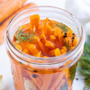 Carrots and dill are in a brining solution in a jar.
