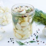 Garlic, dill, and pepper is combined in a jar with a brining solution.
