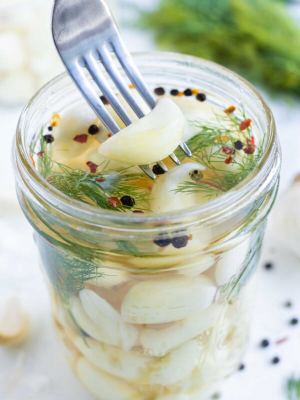A fork scoops a piece of pickled garlic out of a jar.