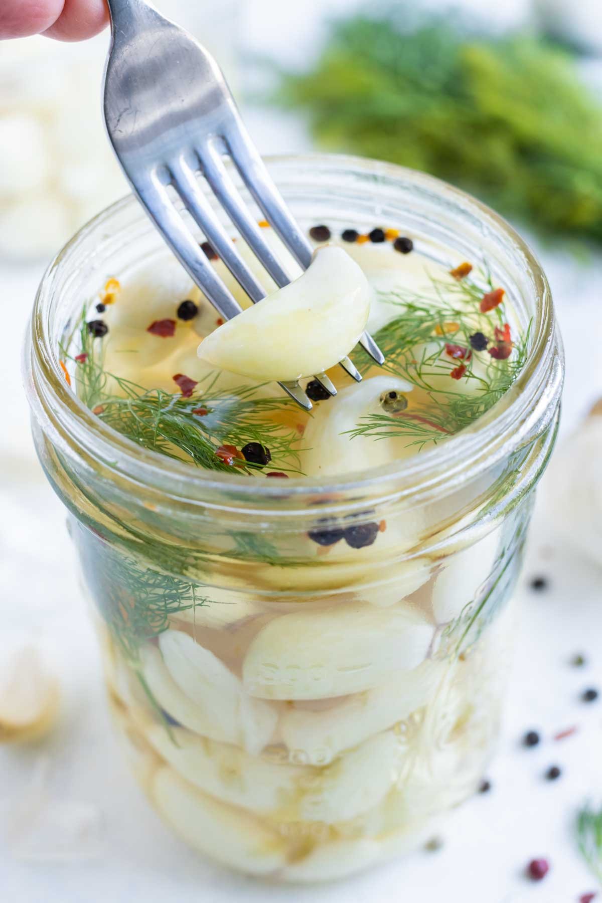 A fork scoops a piece of pickled garlic out of a jar.