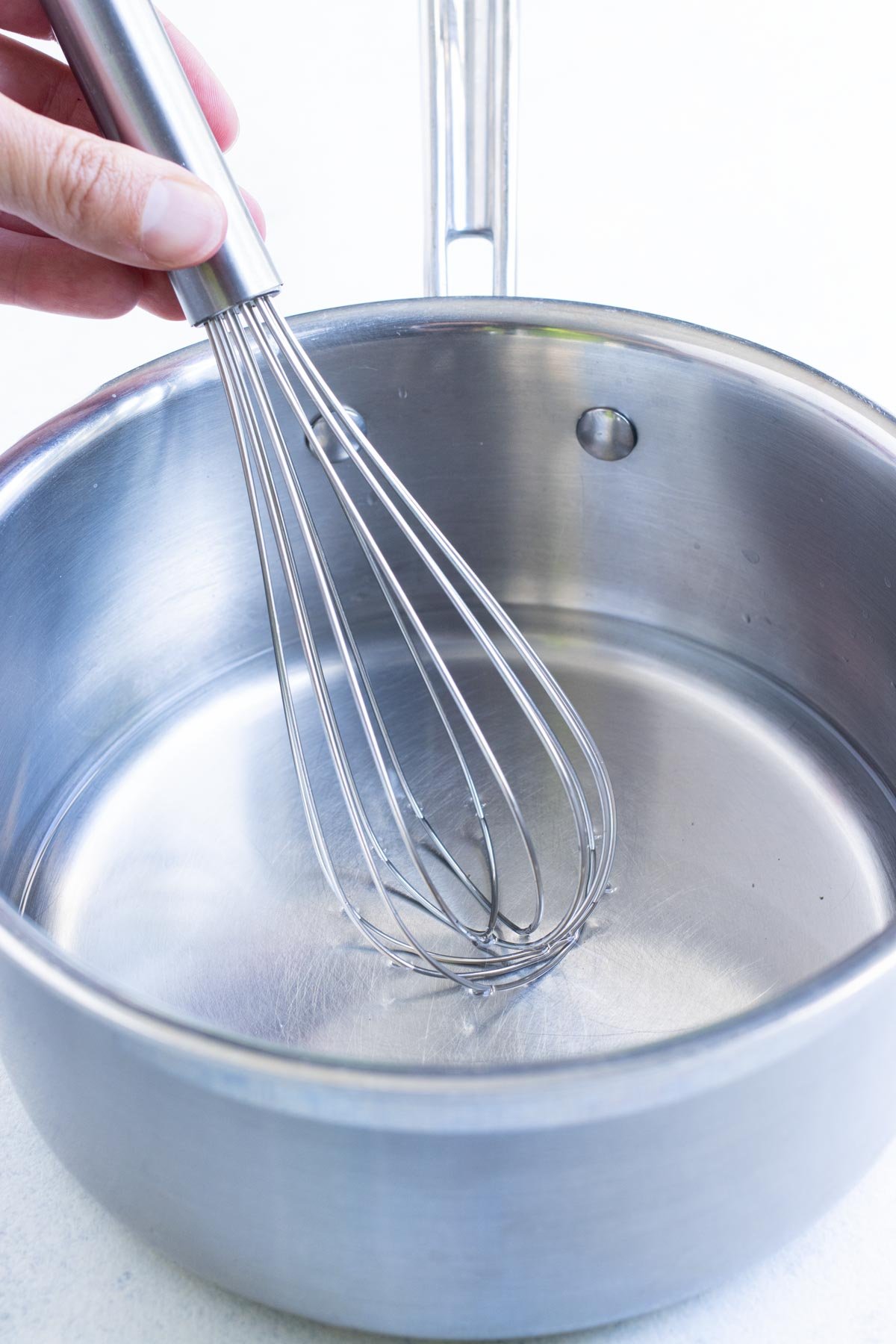 A whisk stirs the brining solution in a saucepan.