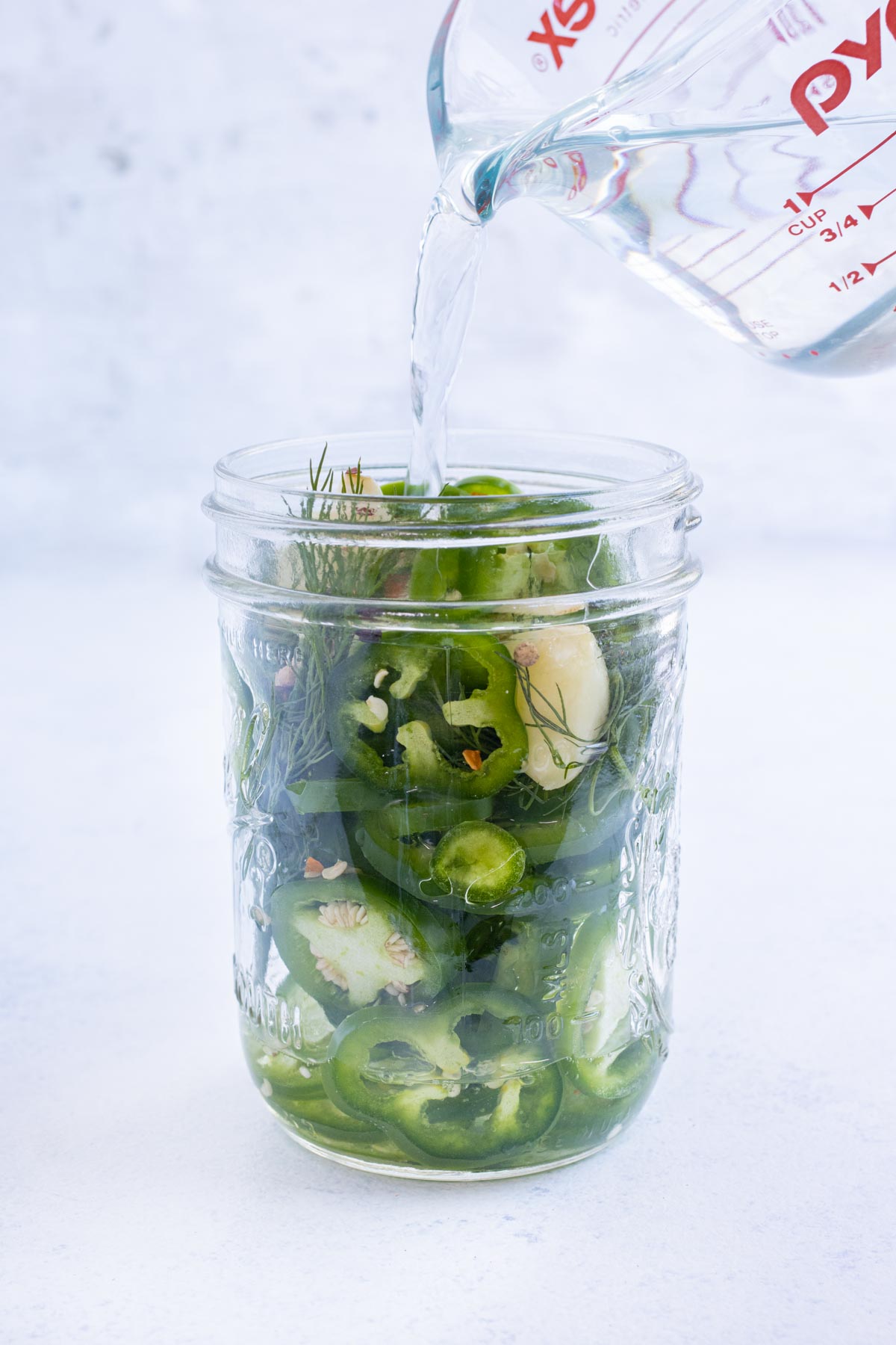 The brining solution is poured over vegetables in a jar.