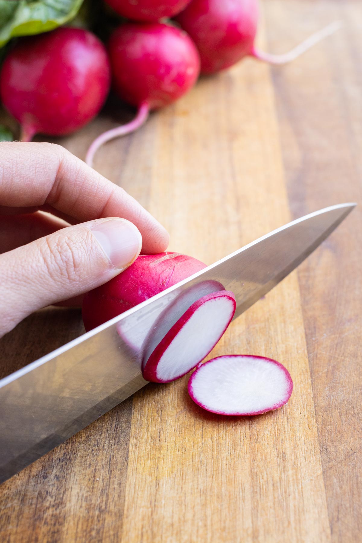 A knife slices radishes on a cutting board.