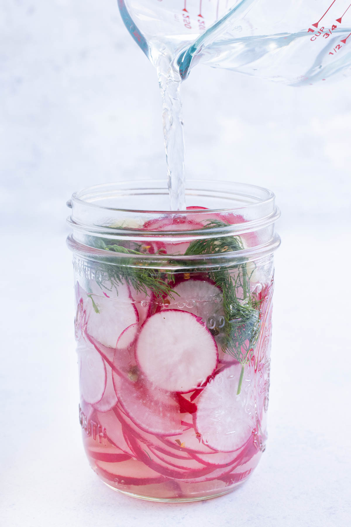 Brining solution is poured over sliced radishes.