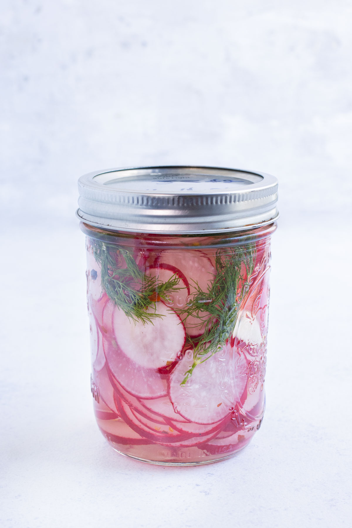 A lid is sealed onto a jar with radishes and brine.