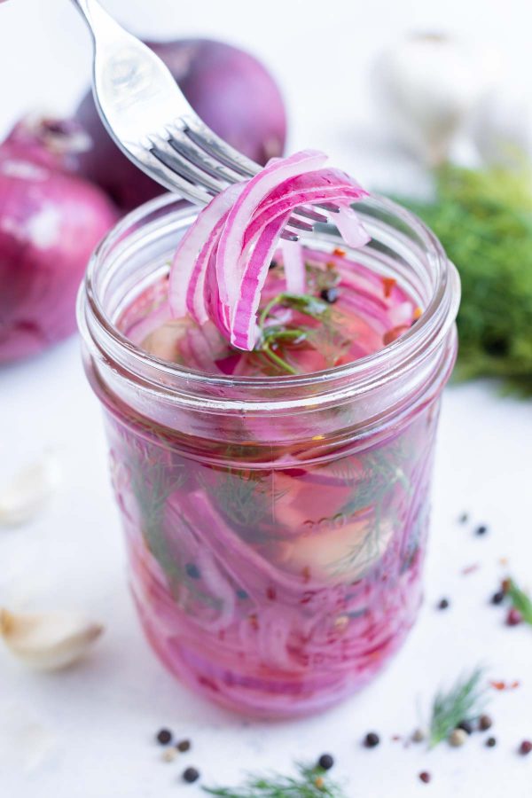A fork scoops some pickled onions out of a jar.