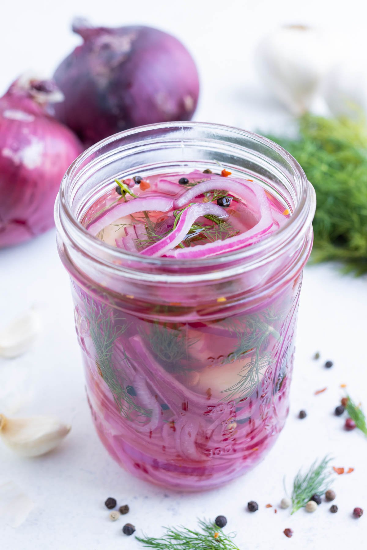 A glass jar with sliced onion, spices, and brining solution.