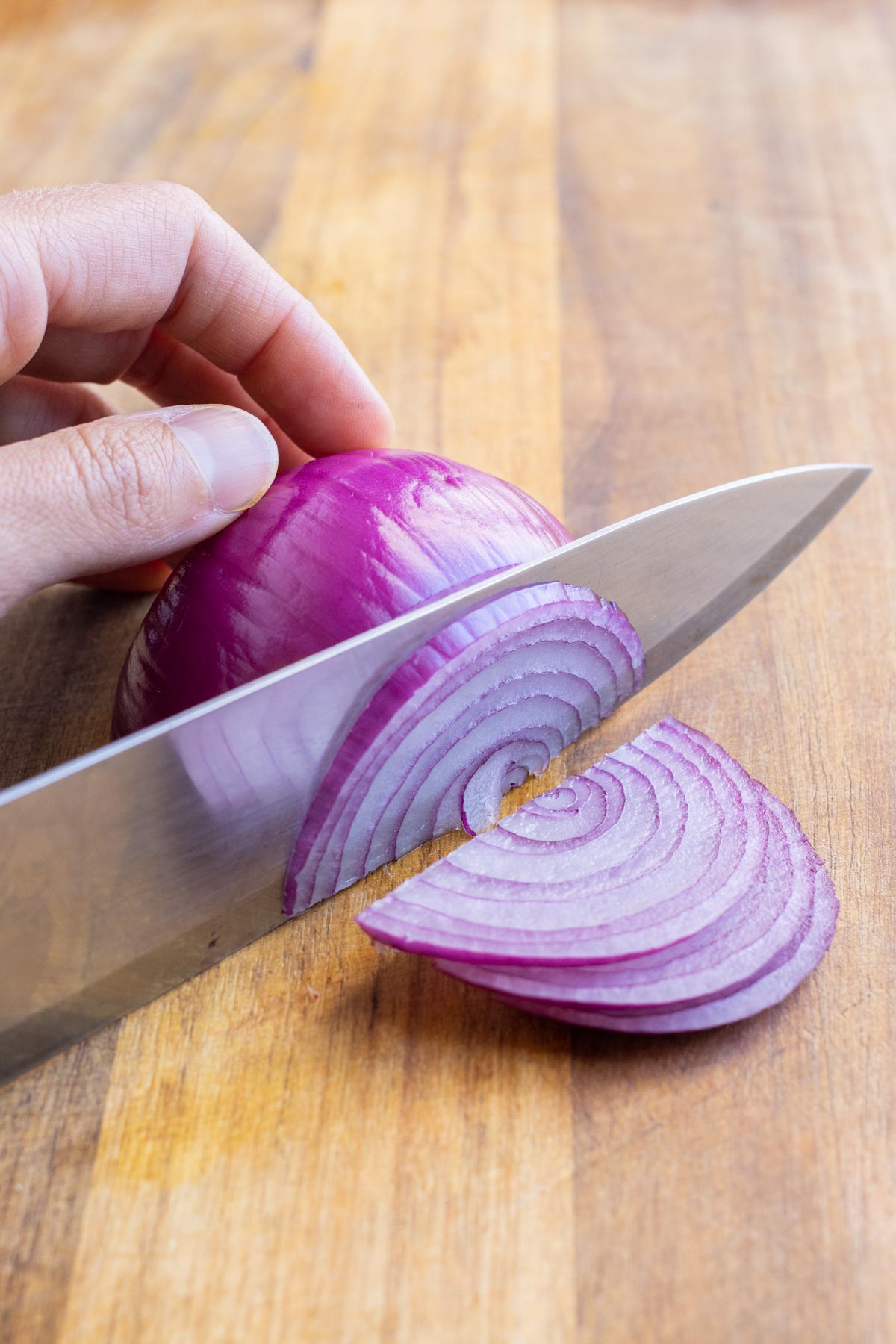 A knife thinly slices a red onion.