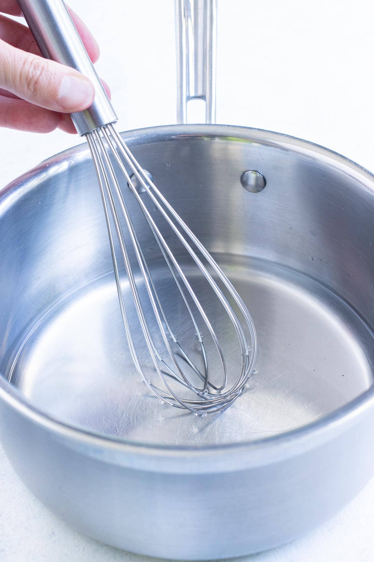 A whisk is used to mix a brining solution in a saucepan.
