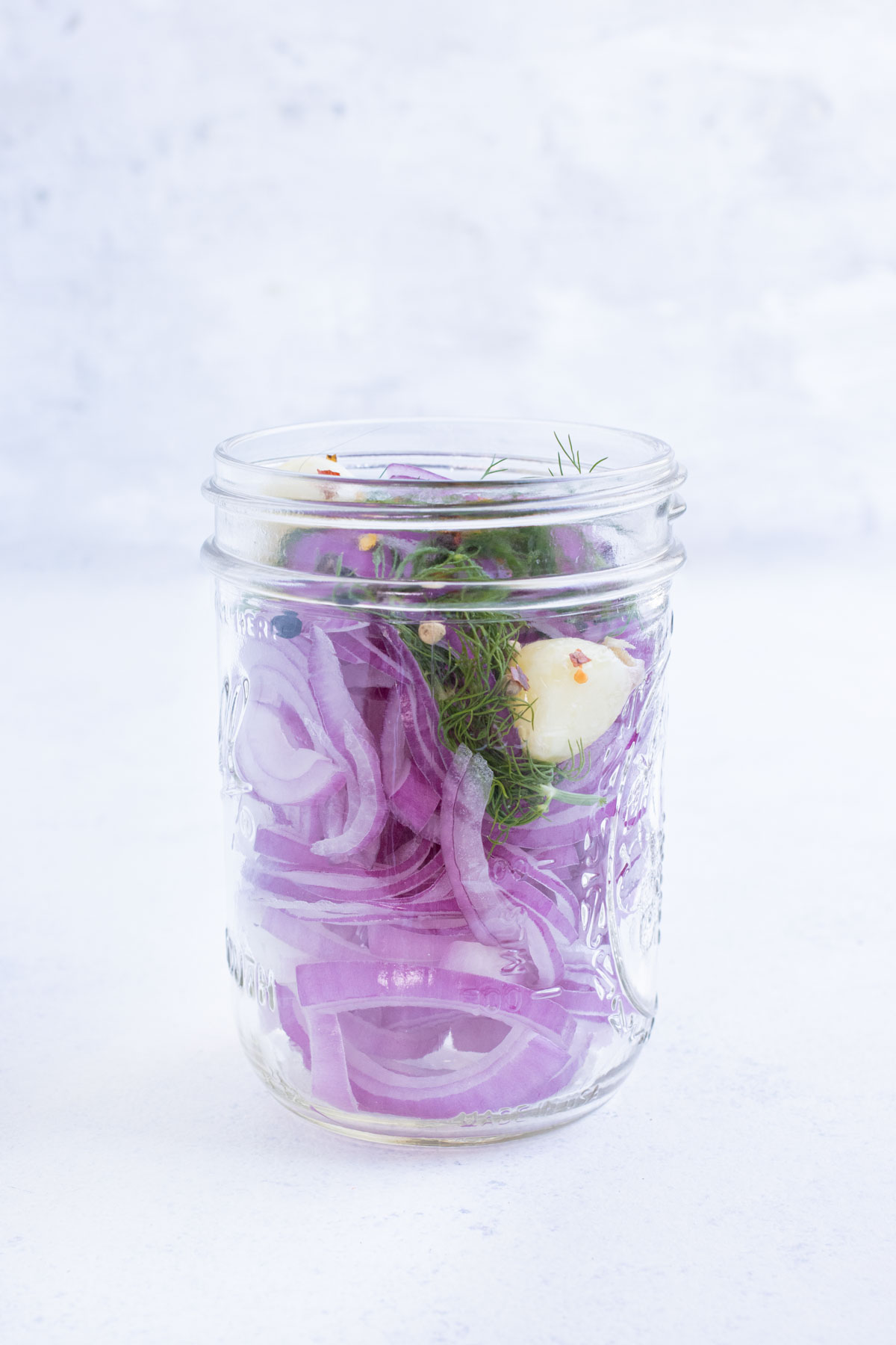 A jar is filled with sliced onions, garlic, and herbs.