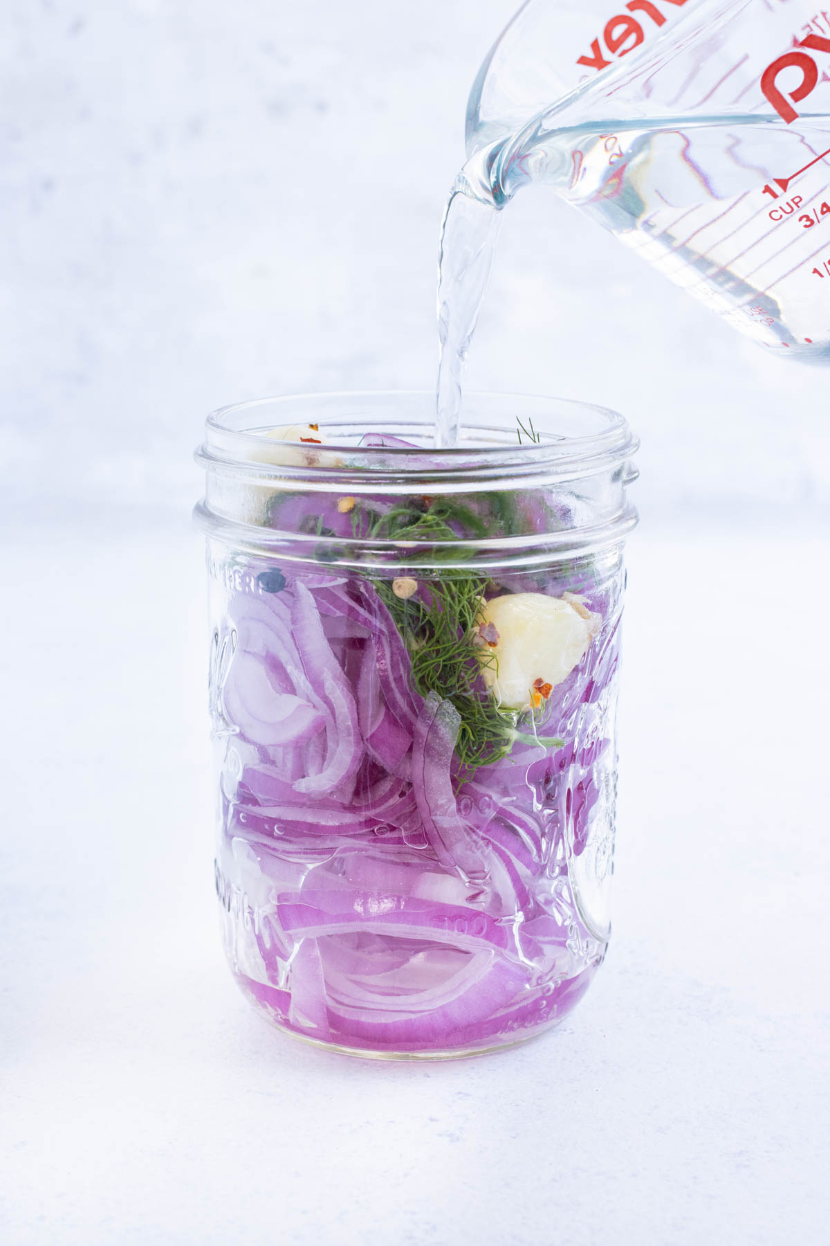 Water is added to a jar with onions and pickling solution.