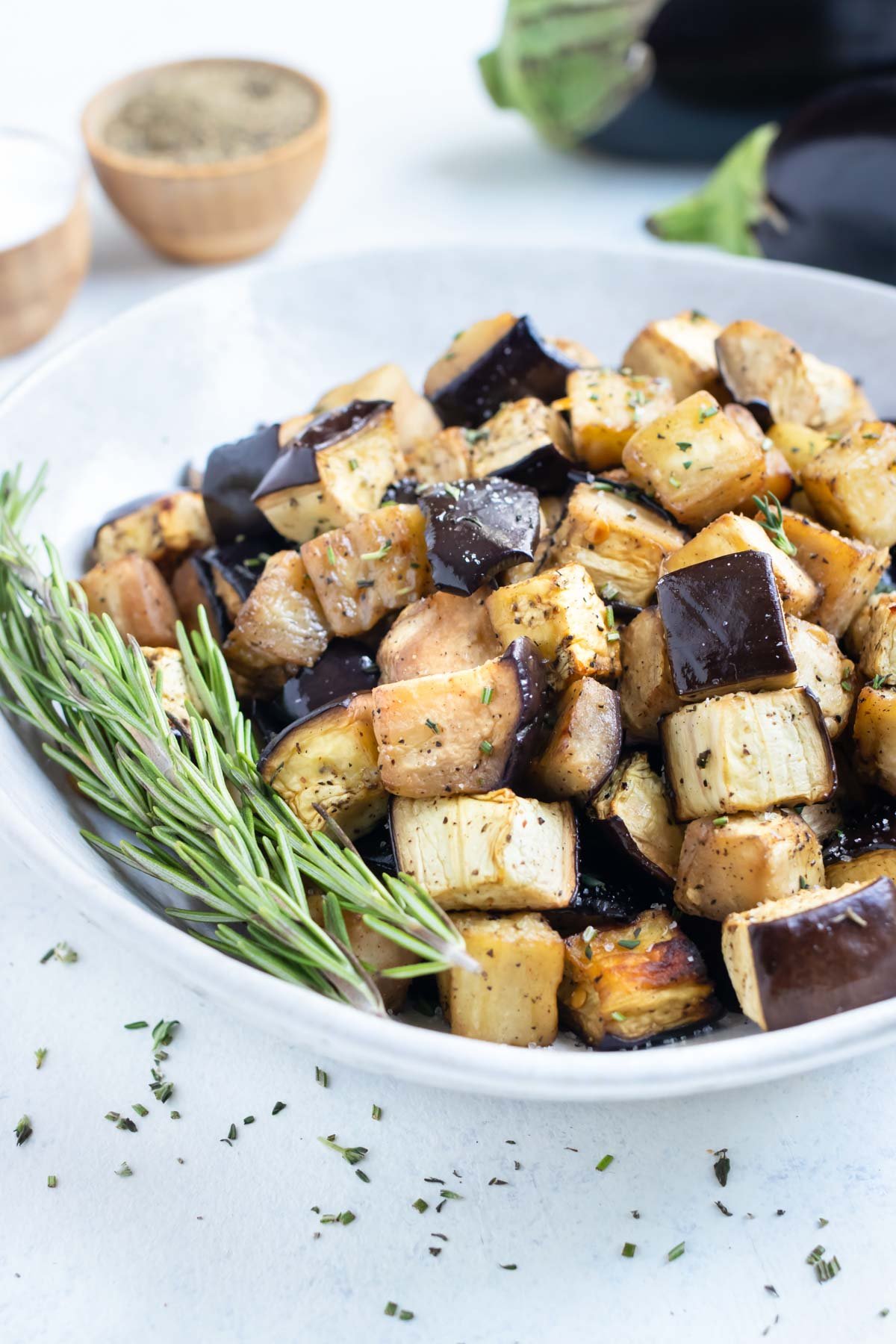 Crispy cubed eggplant is enjoyed from a white bowl with fresh herbs.