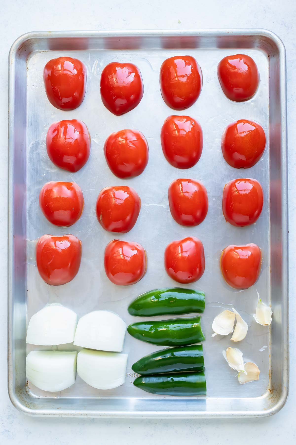 Tomatoes, onion, jalapeño peppers, and garlic are placed on a baking sheet.