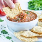 Chips are dipped into a bowl of homemade tomato salsa.