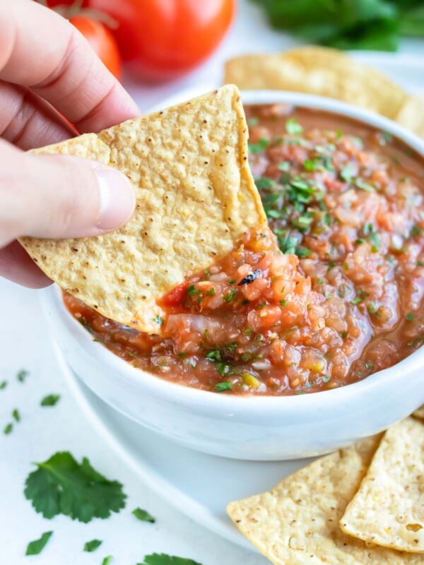 A tortilla chip is dipped into the bowl of roasted tomato salsa.