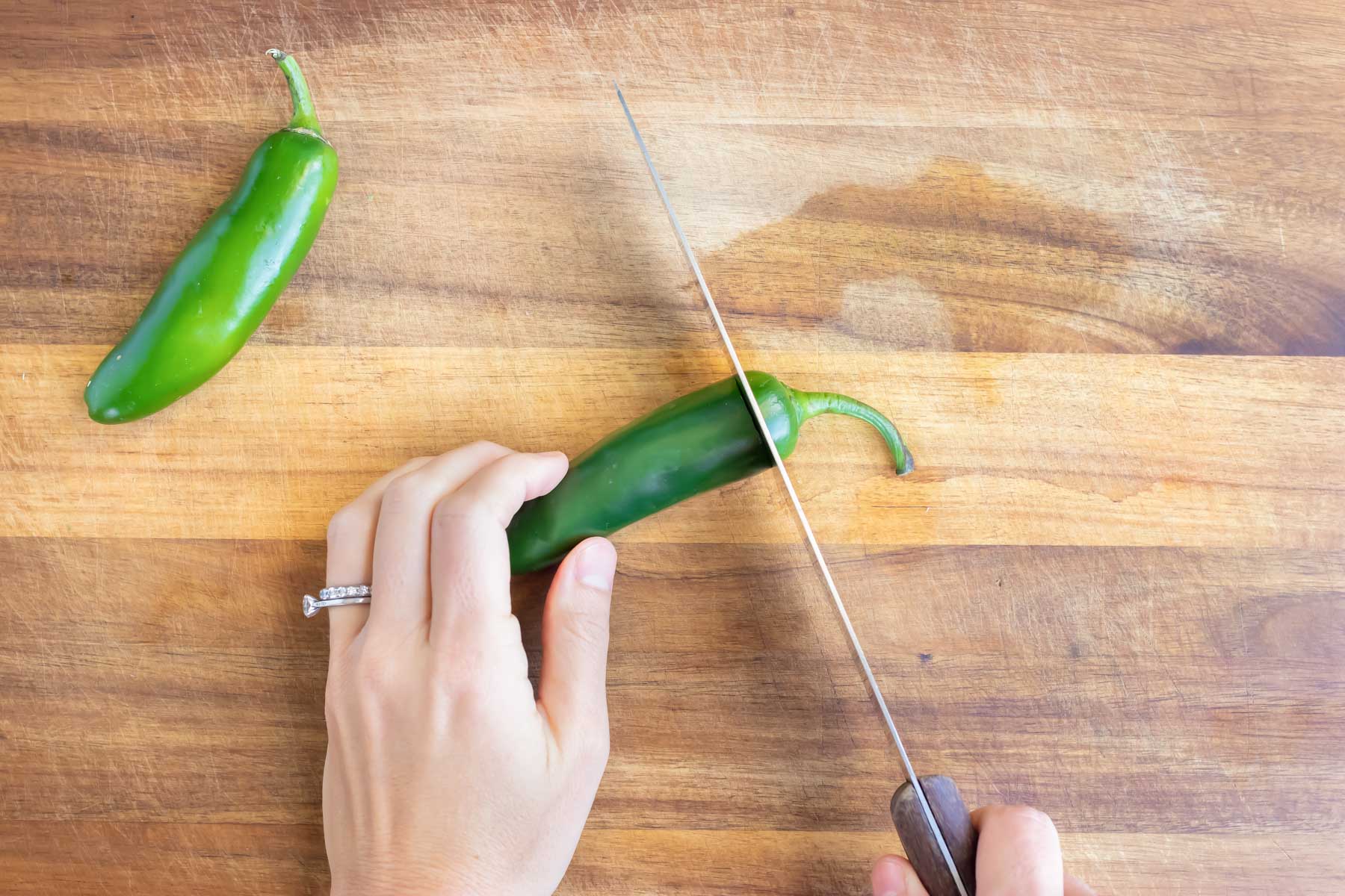 The top of a jalapeno pepper is chopped off with a knife.