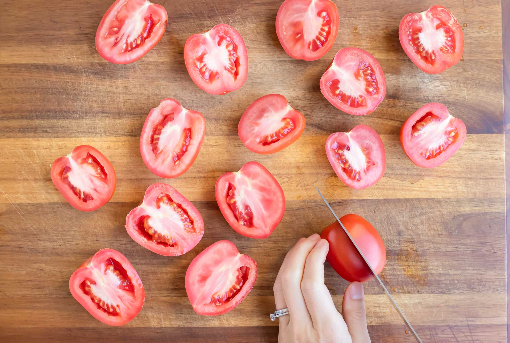 Roma tomatoes are cut in half on a cutting board.