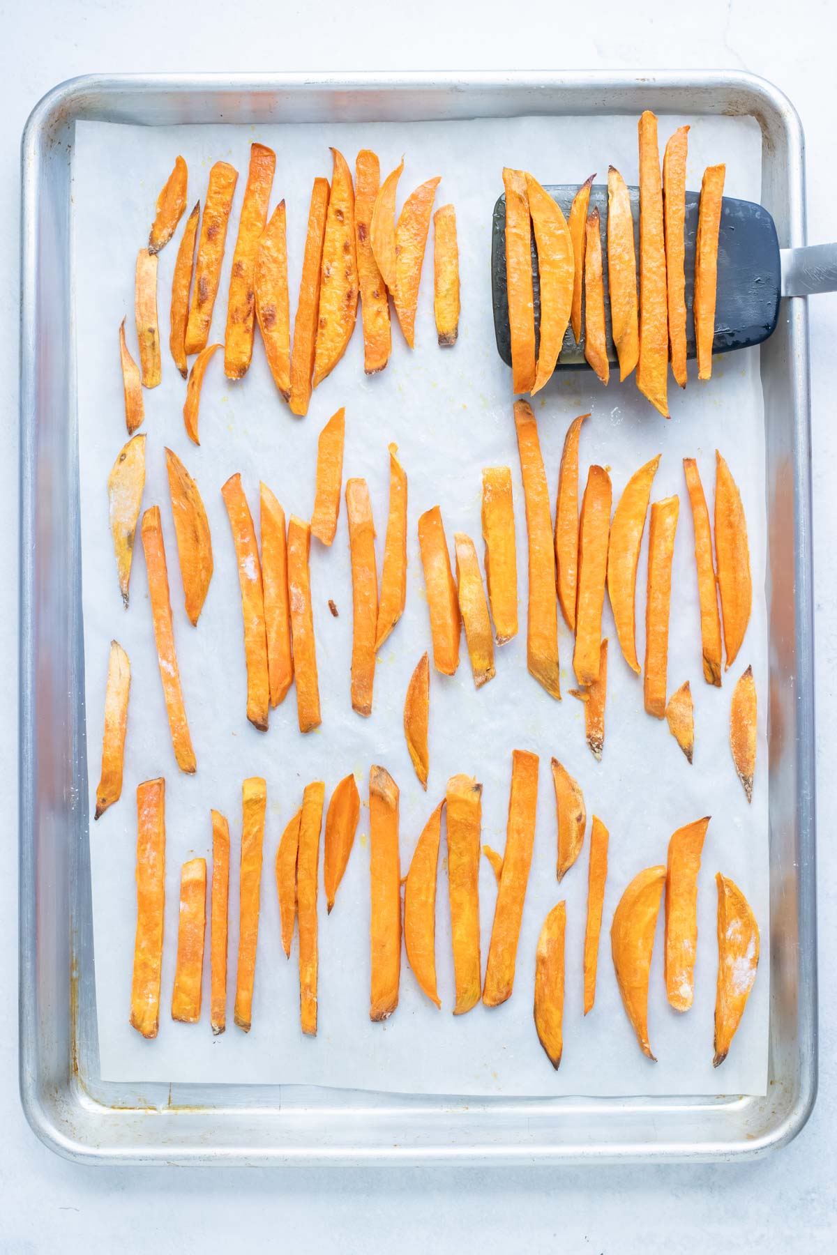 A spatula flipping over sweet potato fries halfway through cooking so they get crispy.
