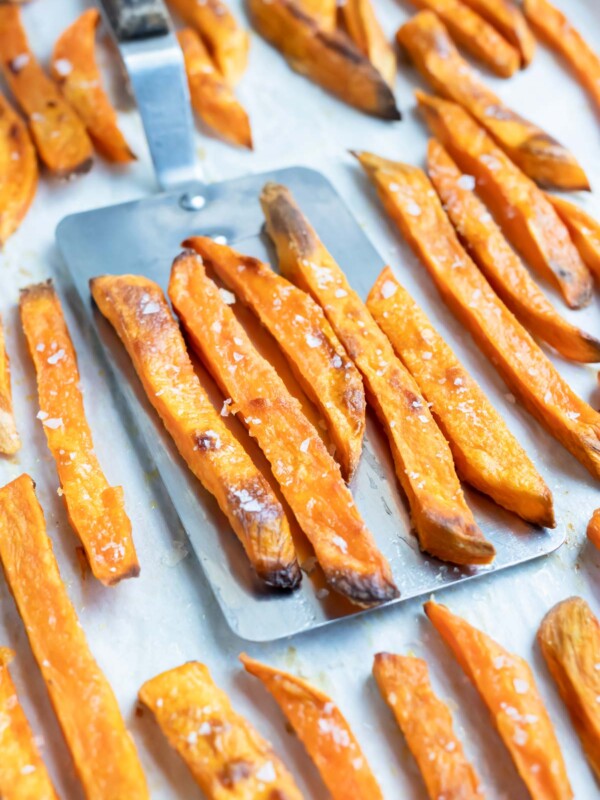 Homemade sweet potato fries are taken off parchment paper after baking.