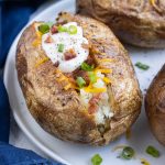 Air fryer baked potatoes are topped with sour cream, cheese, chives, and bacon.