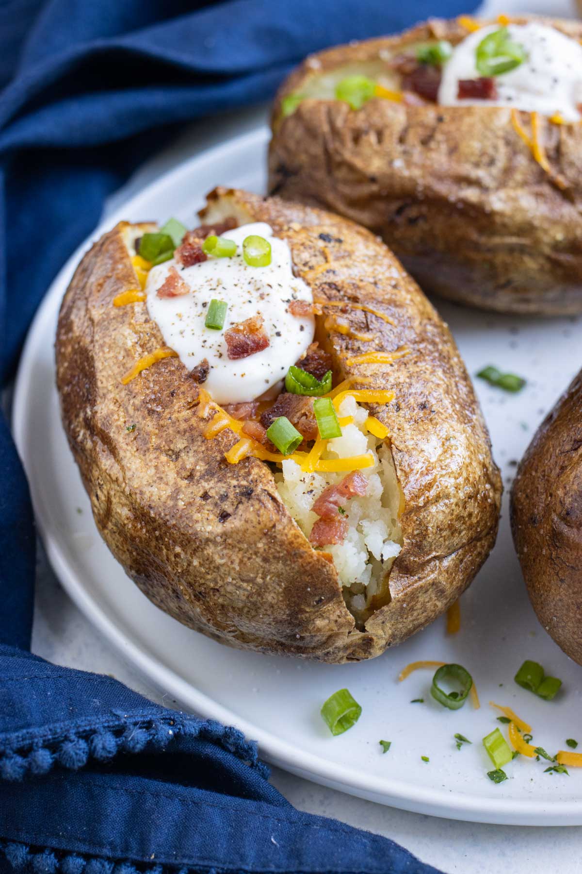 Air fryer baked potatoes are topped with sour cream, cheese, chives, and bacon.