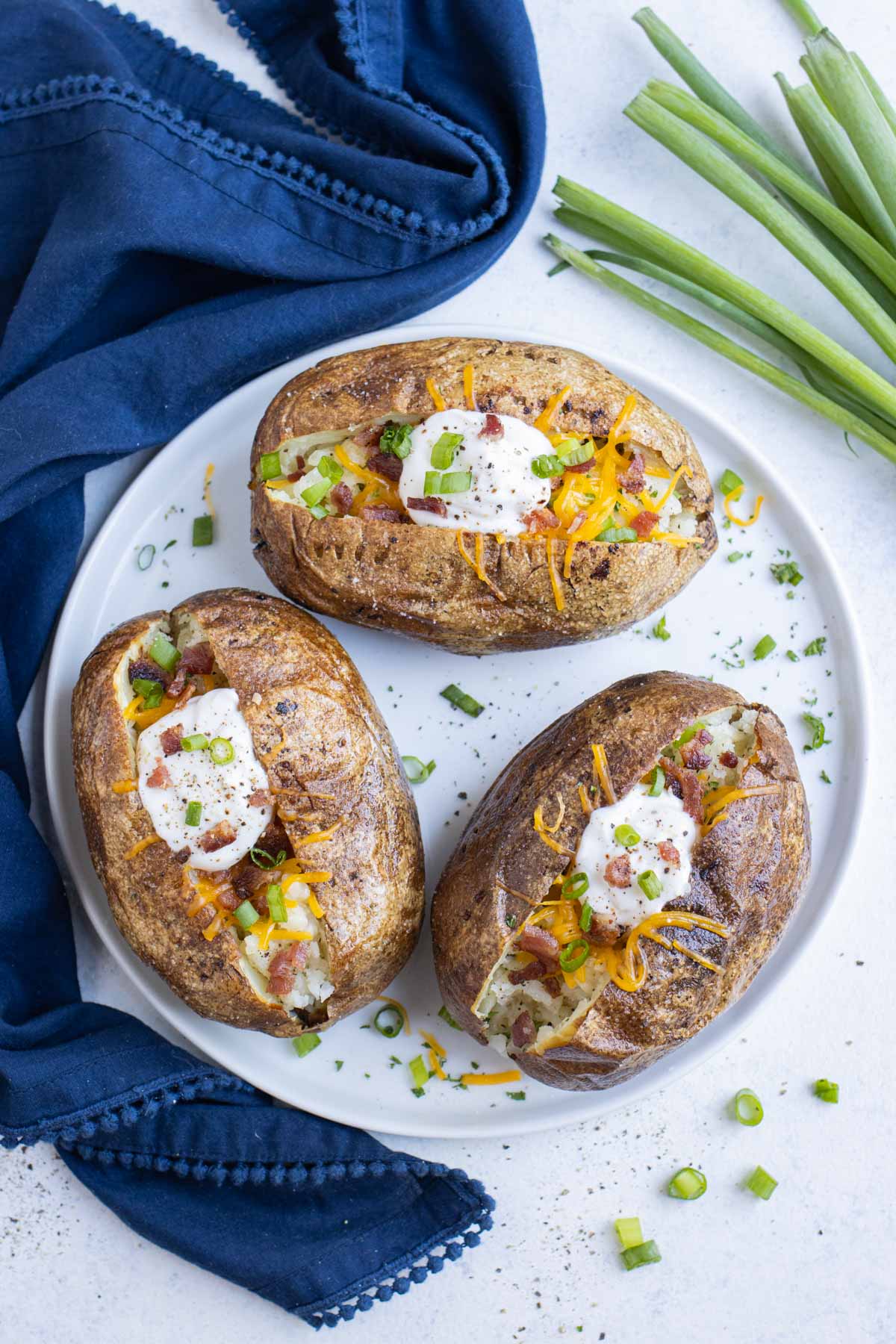 Three baked potatoes are on a plate with a blue napkin.